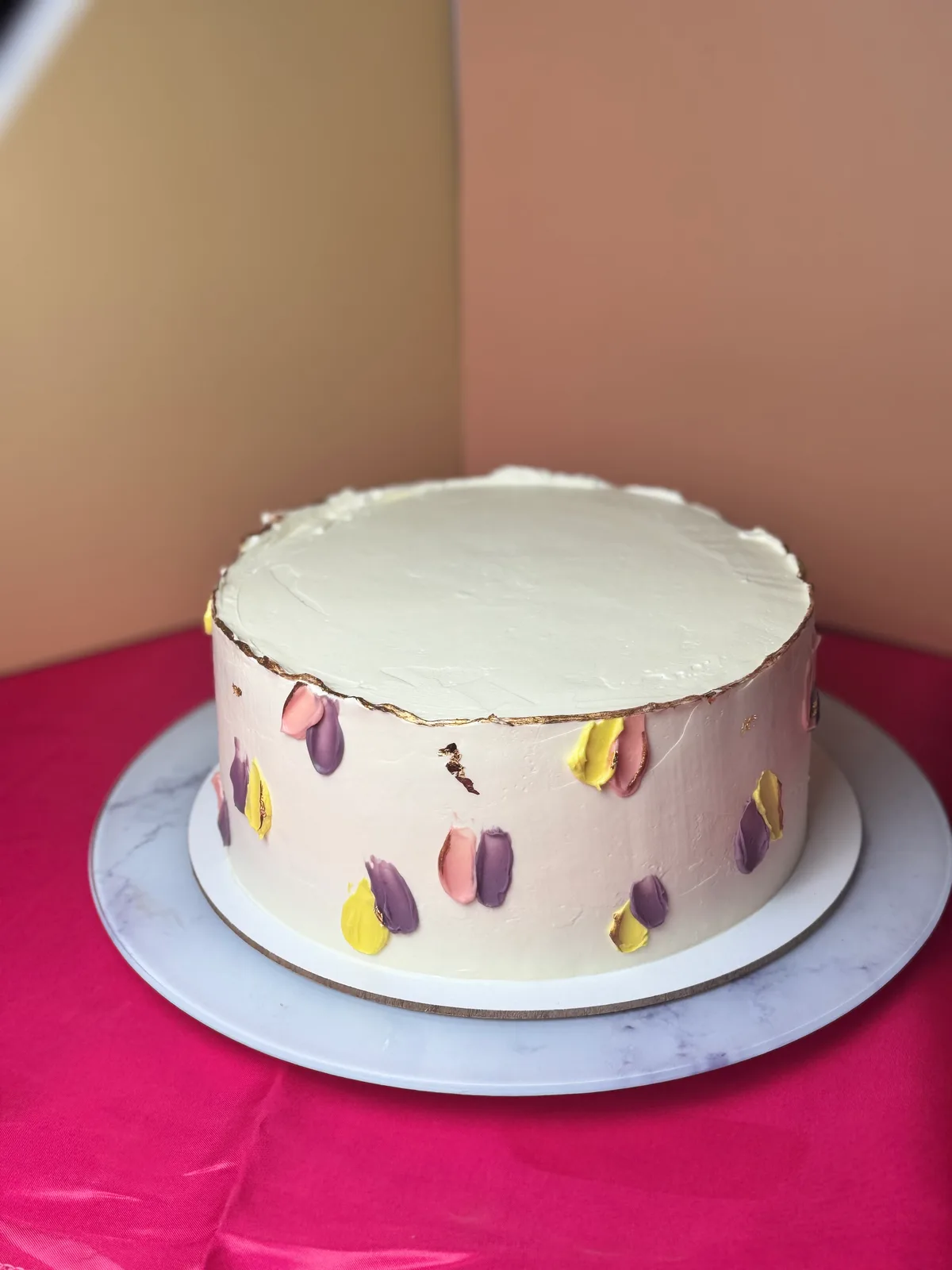 Bolo branco com pinceladas em rosa, lilás e amarelo pastel e borda com folha de ouro