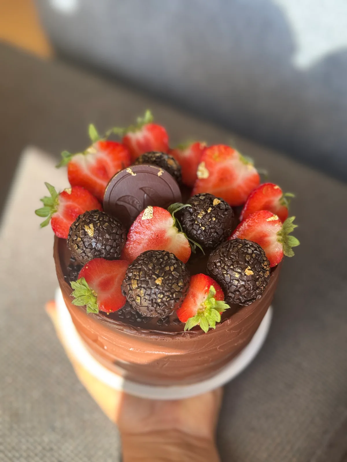 Bolo de chocolate com morangos frescos, brigadeiros com flocos dourados e um medalhão de chocolate no topo