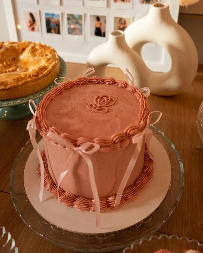 Bolo vintage rosa antigo com bordas de buttercream, laços de fita de cetim e uma rosa desenhada no topo